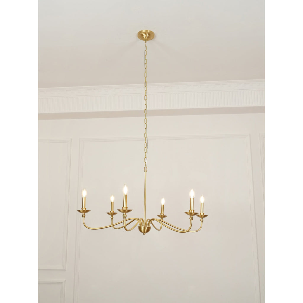A Clérachic brass chandelier lit with candle bulbs, hung low from its chain below a cornice in a pale room.
