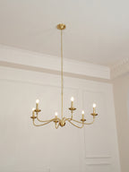 A Clérachic brass chandelier seen from below, lit, with bulbs at varied heights against pale wall panels.