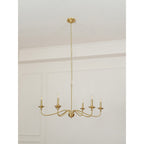 A Clérachic brass chandelier with a long rod and chain, unlit, hanging in a room with a white moulded wall.