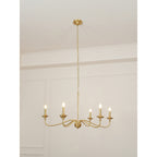 A Clérachic brass chandelier lit under a high ceiling, with moulded wall panels and a thin chain above.