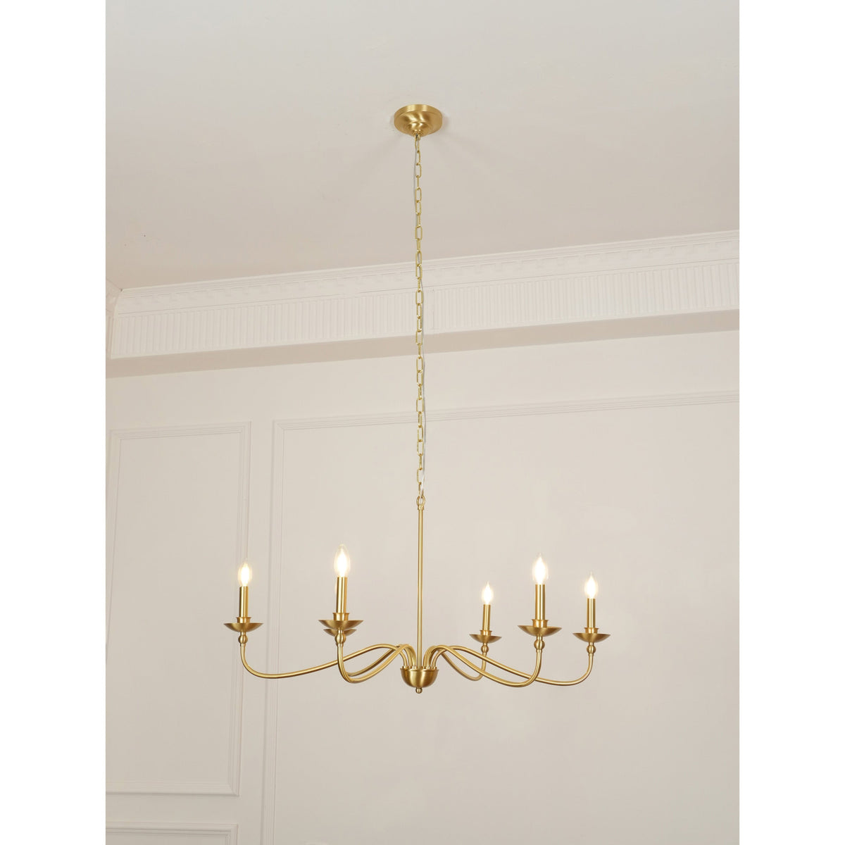 A Clérachic brass chandelier lit under a high ceiling, with moulded wall panels and a thin chain above.