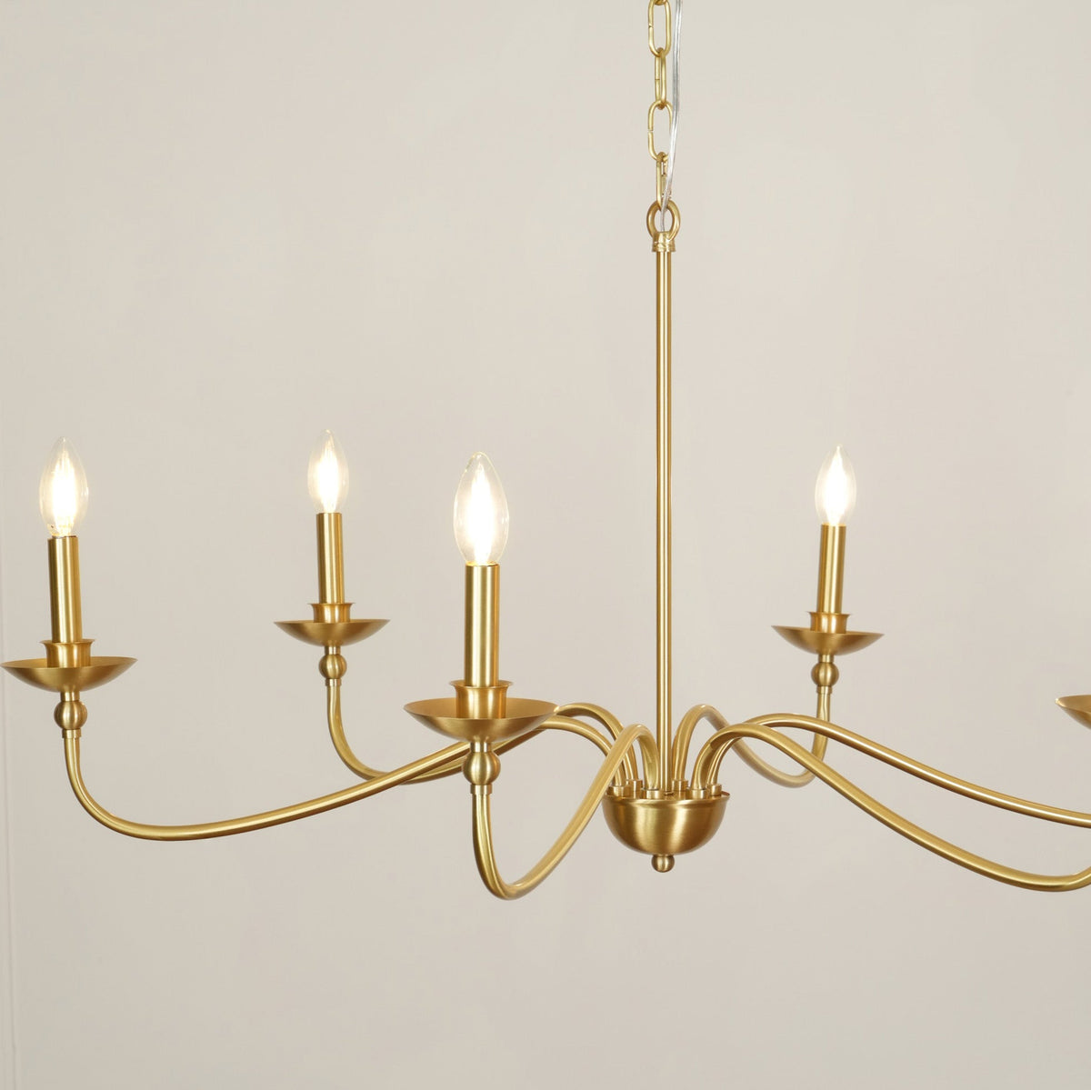 Close view of the lit candle-style bulbs and curved brass arms on this Clérachic chandelier, with the rod above.