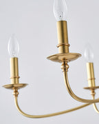 Close view of a candle bulb, a brass cup and a curved arm on this Clérachic chandelier, against a pale grey backdrop.