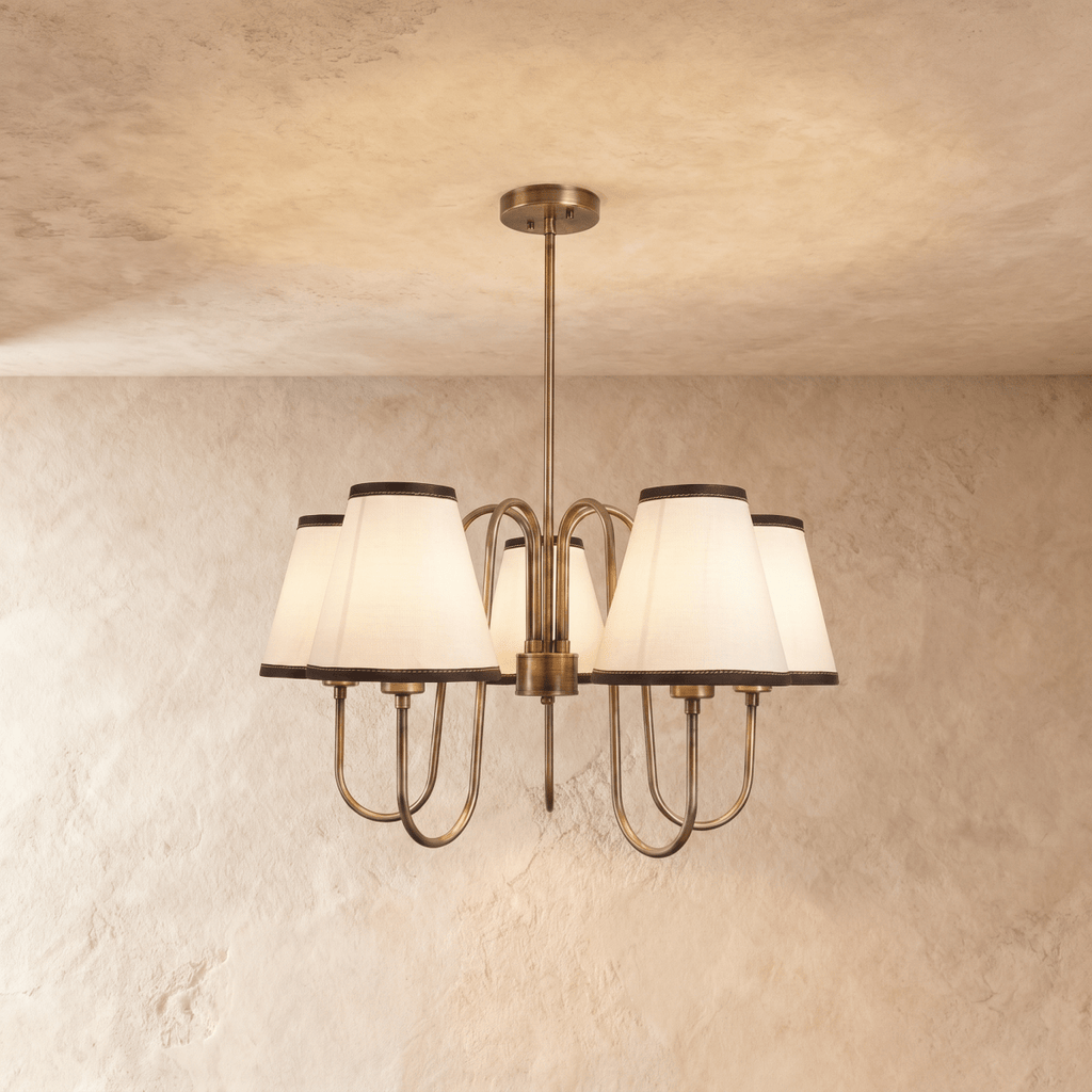 Clérachic chandelier in vintage brass with five ivory shades trimmed in charcoal, hung from a plaster ceiling.
