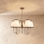 Clérachic chandelier in vintage brass with five ivory shades trimmed in charcoal, hung from a plaster ceiling.