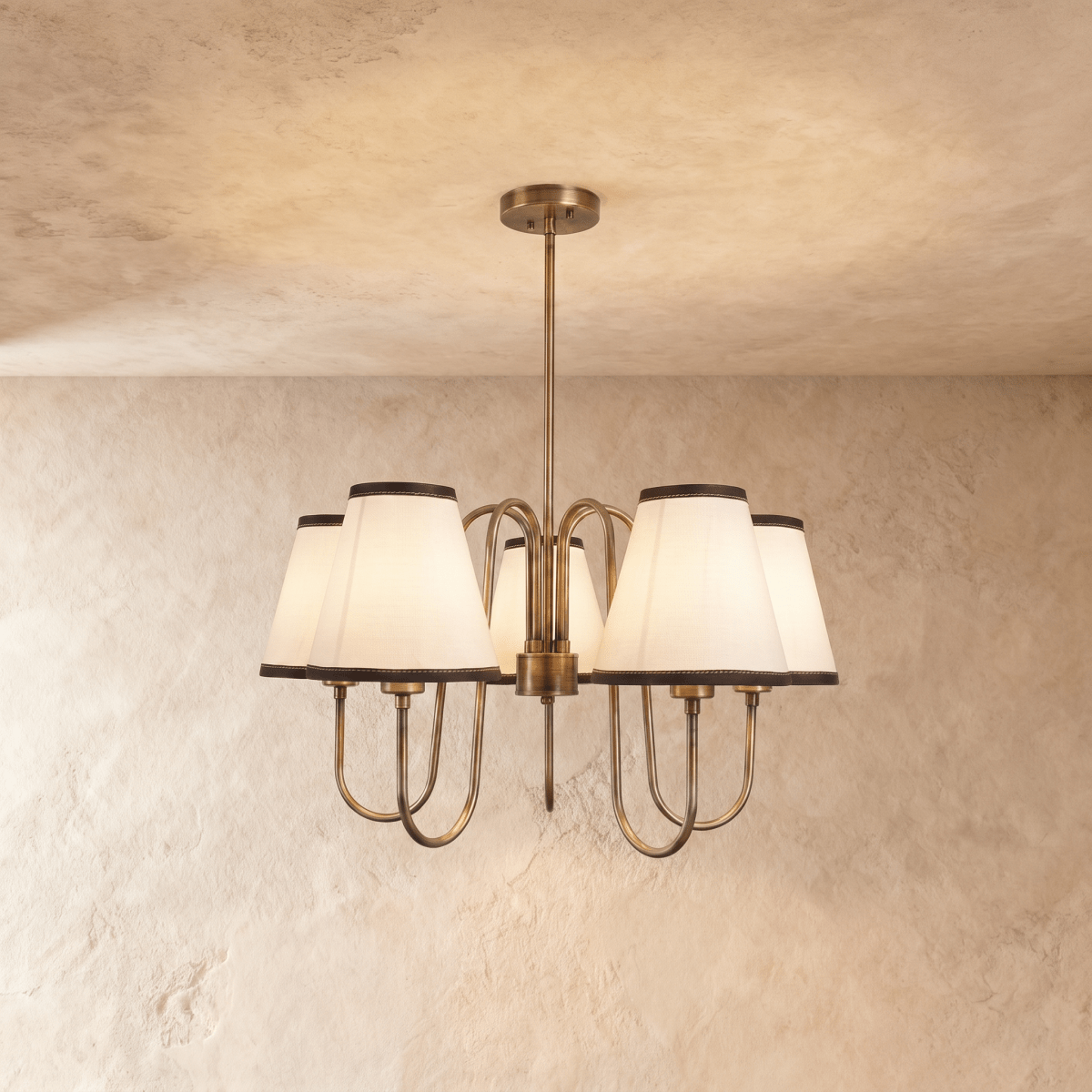 Clérachic chandelier in vintage brass with five ivory shades trimmed in charcoal, hung from a plaster ceiling.