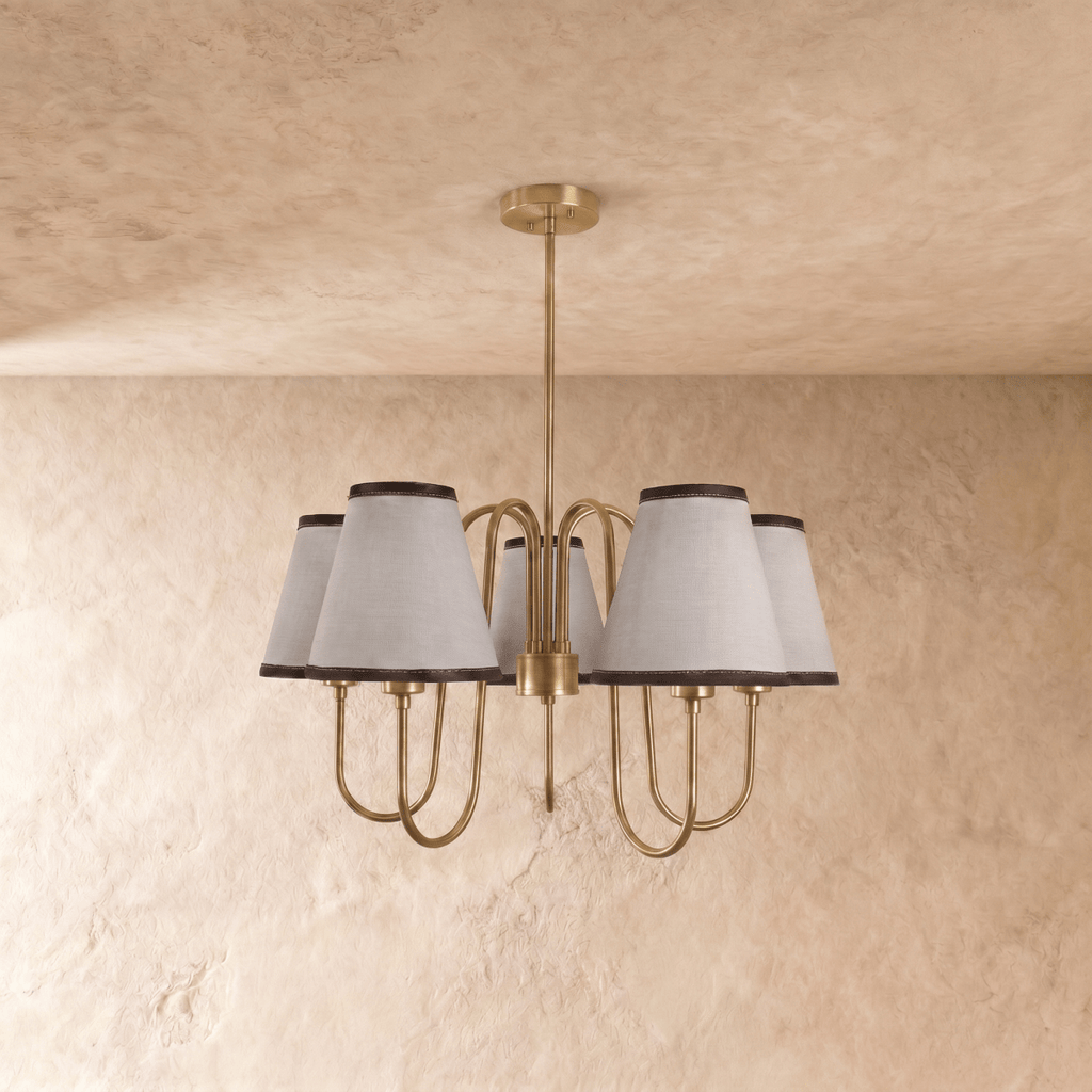 A polished brass Clérachic chandelier viewed from below, its five ivory shades glowing warmly.