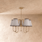 A polished brass Clérachic chandelier viewed from below, its five ivory shades glowing warmly.