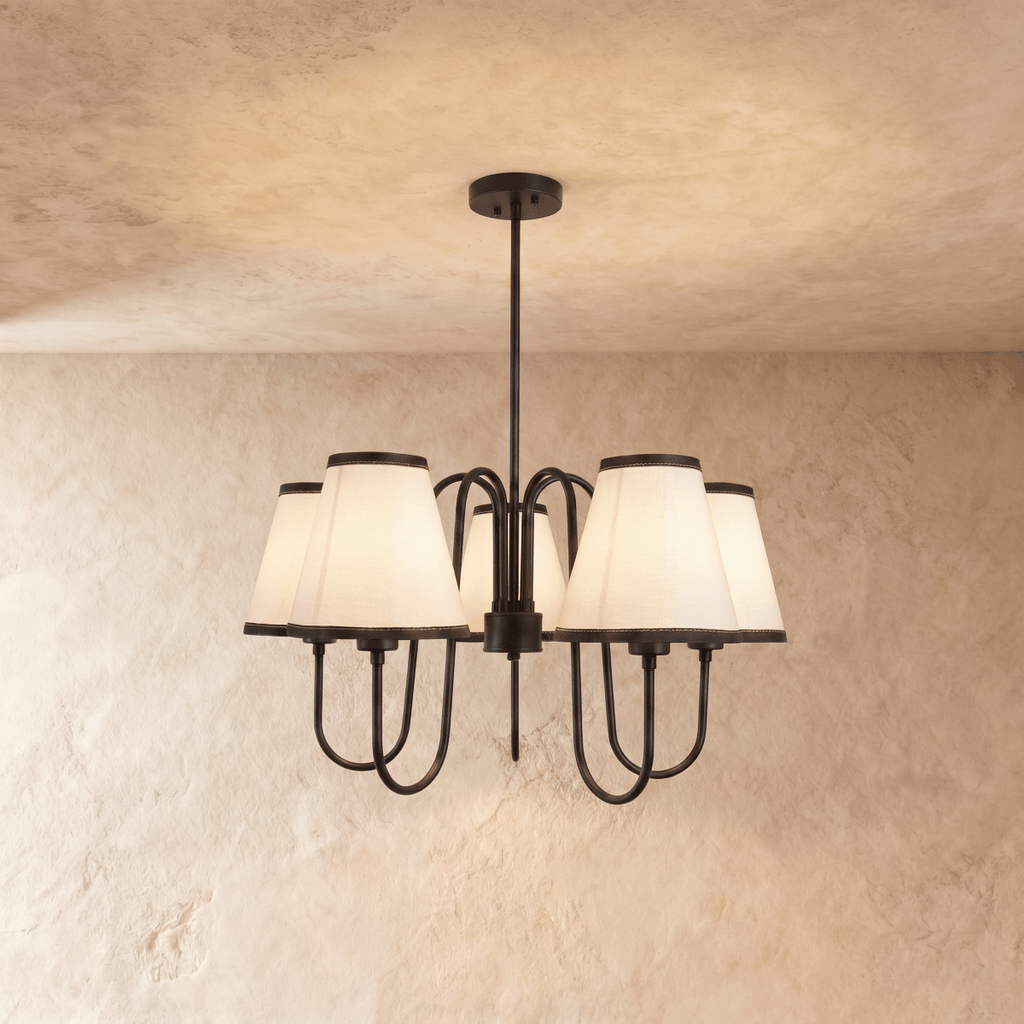 Clérachic chandelier in matte black, five ivory shades trimmed in dark piping against a plaster wall.