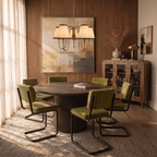 A brass Clérachic chandelier hangs above a round wood table surrounded by olive velvet chairs.