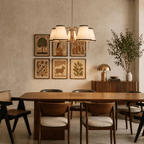 A brass Clérachic chandelier lights a dining table beneath a gallery wall of framed botanical prints.