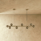 Clérachic brass linear chandelier with smokey grey glass globes hanging from twin round ceiling canopies.