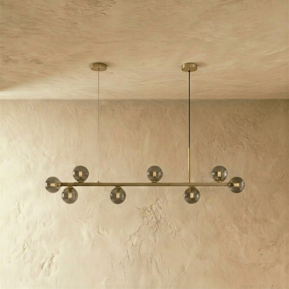 Clérachic brass linear chandelier with smokey grey glass globes hanging from twin round ceiling canopies.