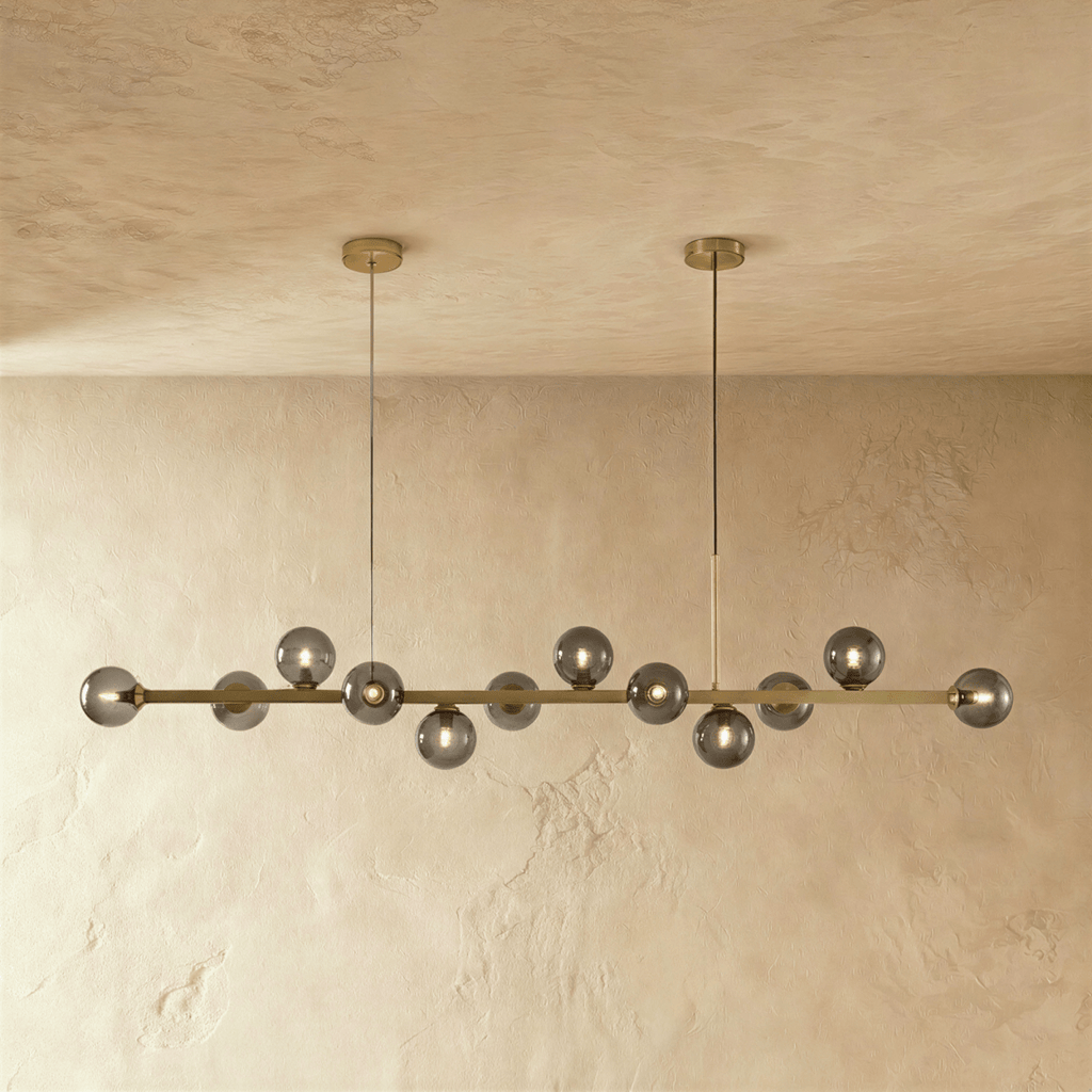 Clérachic linear chandelier shows a full row of lit smokey grey glass globes along an extended brass bar.