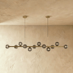 Clérachic linear chandelier shows a full row of lit smokey grey glass globes along an extended brass bar.