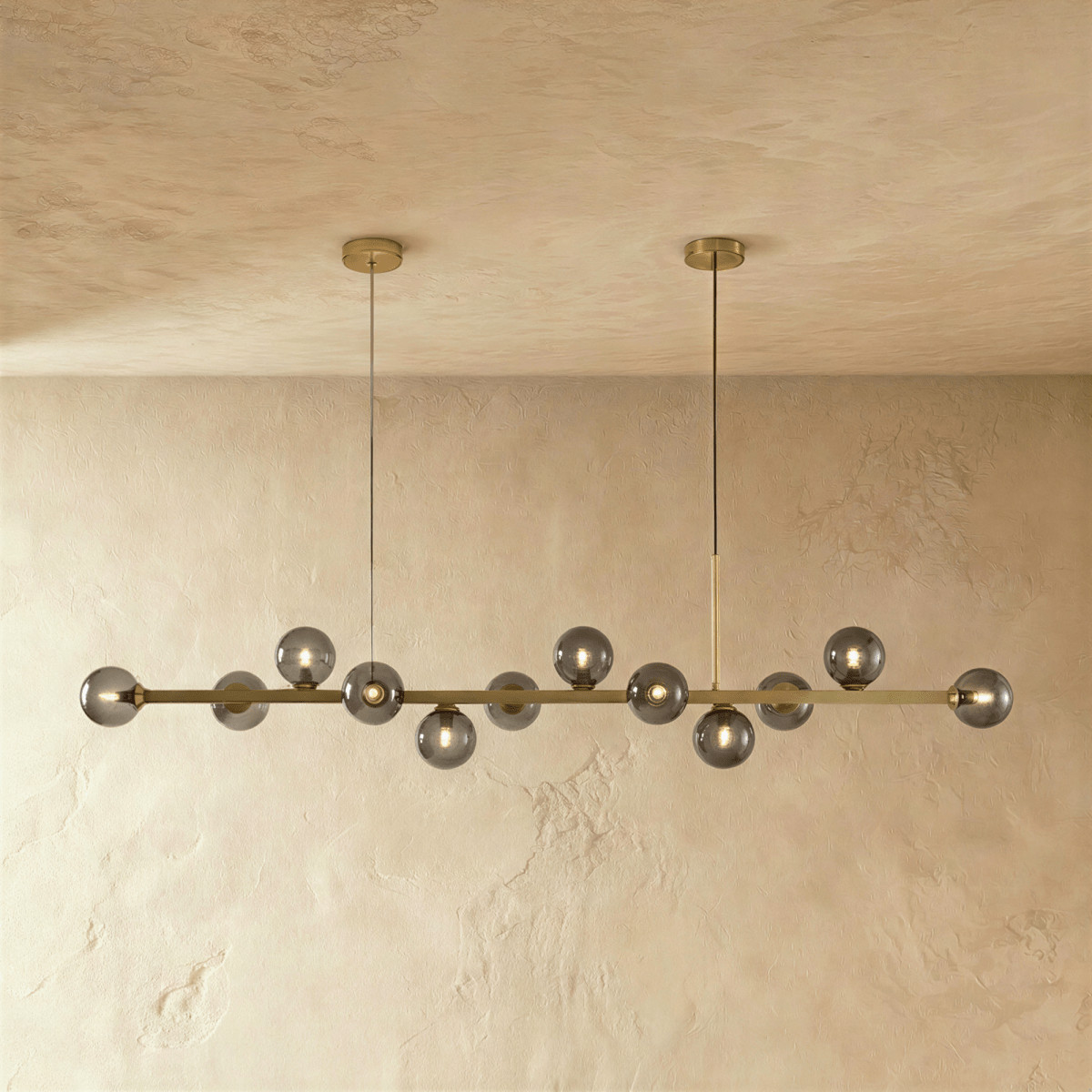 Clérachic linear chandelier shows a full row of lit smokey grey glass globes along an extended brass bar.