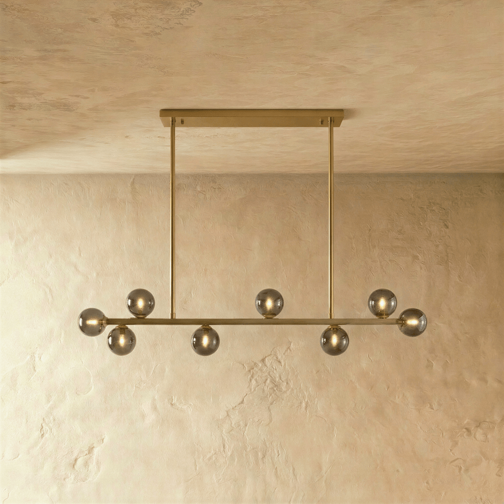 Clérachic linear chandelier hangs from a single brass horizontal bar plate, smokey grey glass globes unlit.