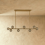 Clérachic linear chandelier hangs from a single brass horizontal bar plate, smokey grey glass globes unlit.