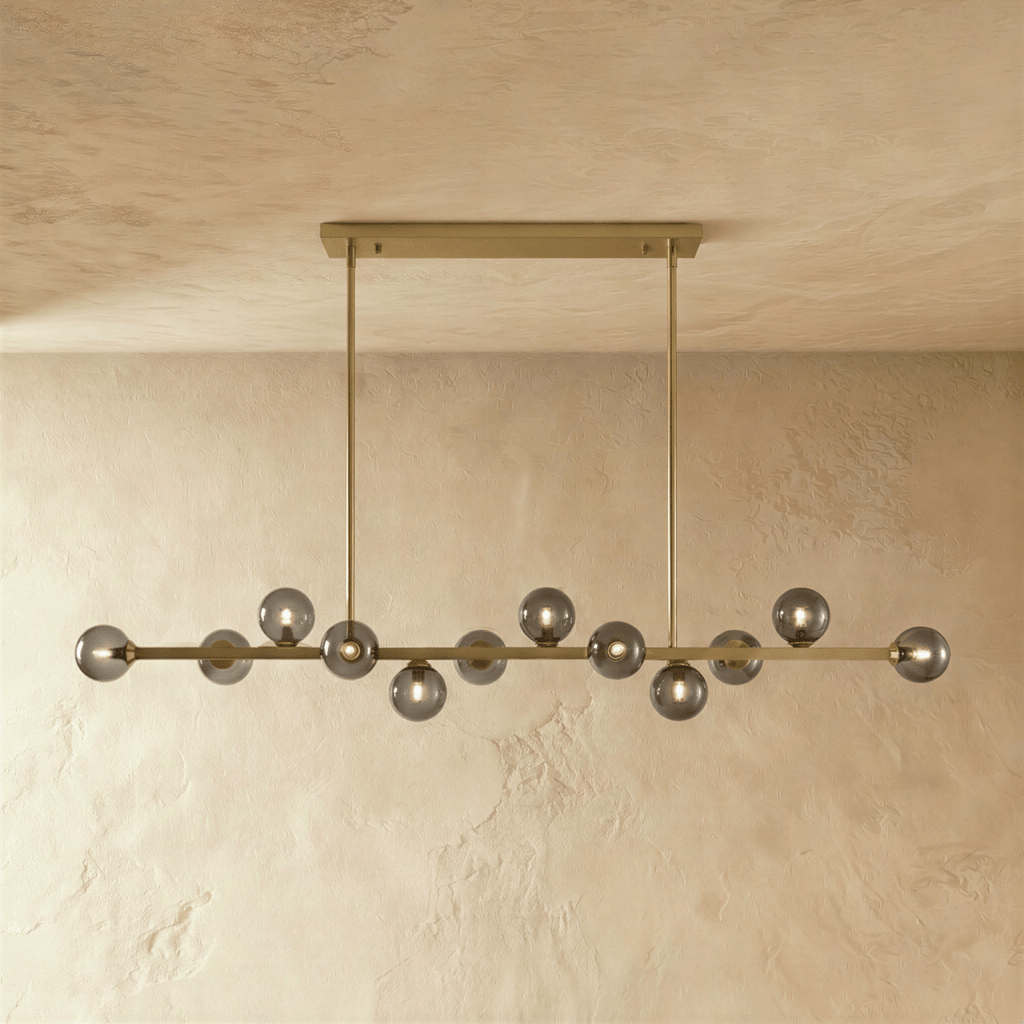 Clérachic linear chandelier shows a dense row of clear glass globes suspended from a horizontal bar plate.