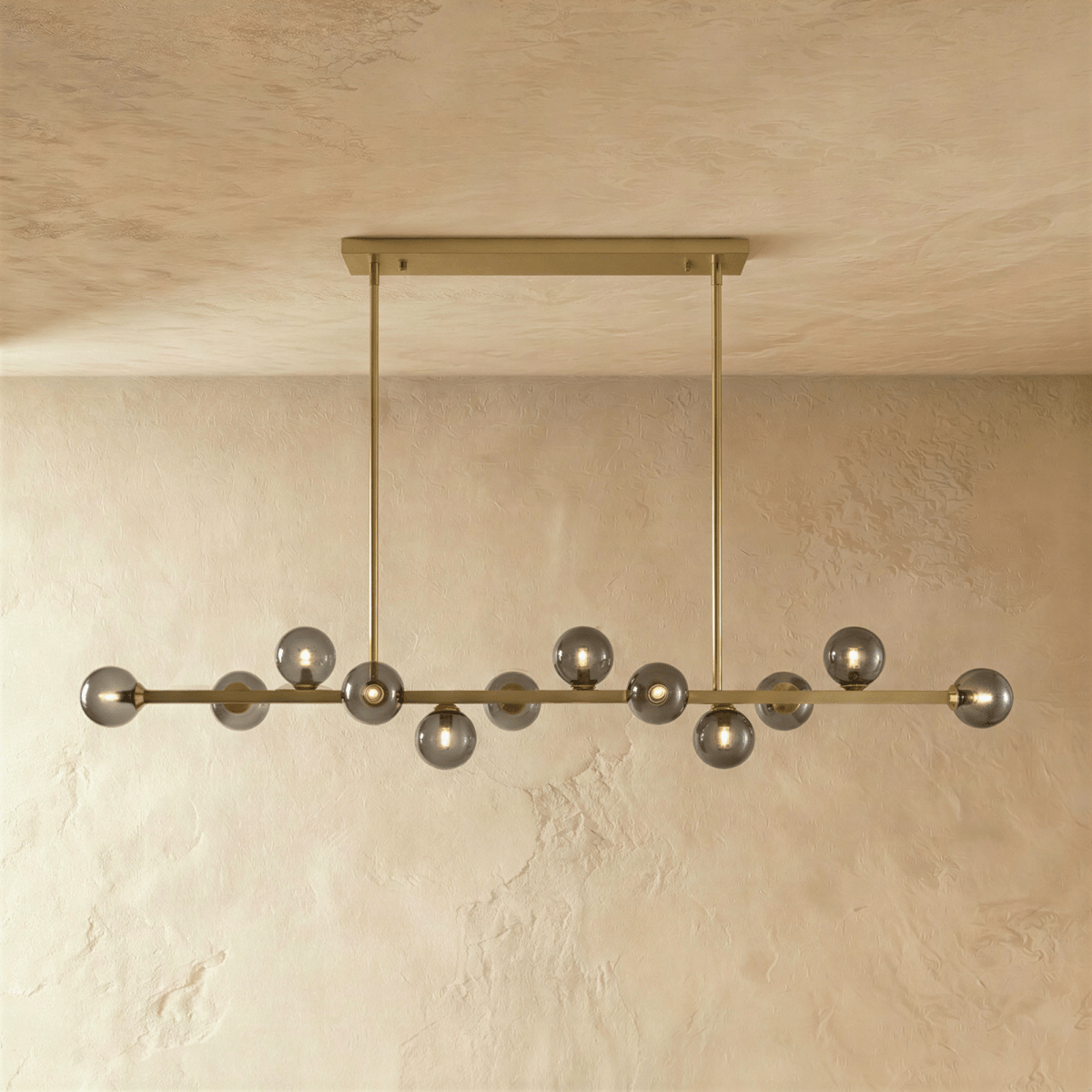 Clérachic linear chandelier shows a dense row of clear glass globes suspended from a horizontal bar plate.