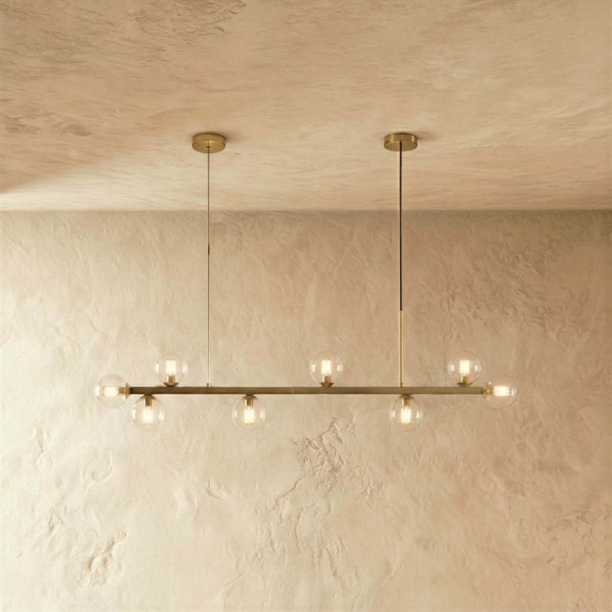 Clérachic brass linear chandelier, clear glass globes lit warm, hanging from two round ceiling canopies.