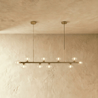 Clérachic linear chandelier at its longest, clear glass globes lit warm along the full brass bar.