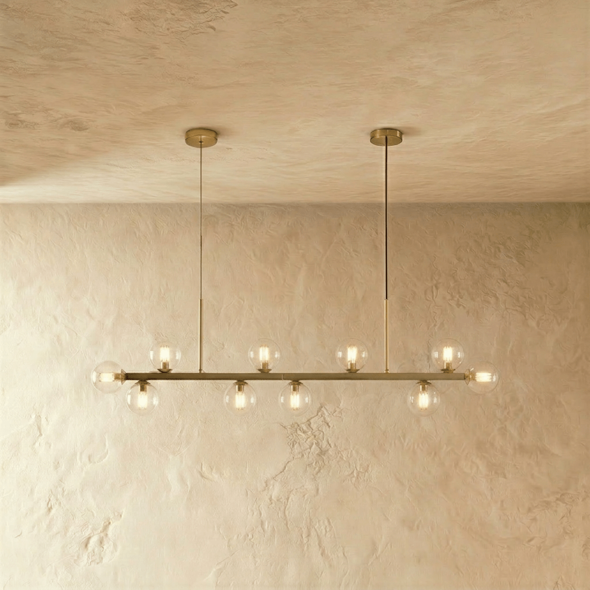 Clérachic linear chandelier at its longest, clear glass globes lit warm along the full brass bar.