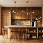 Clérachic linear chandelier lights a wood kitchen island, clear glass globes glowing above the marble counter.