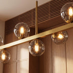 Clérachic chandelier detail shows clear glass globes and brass stems meeting the bar, filament bulbs lit warm.