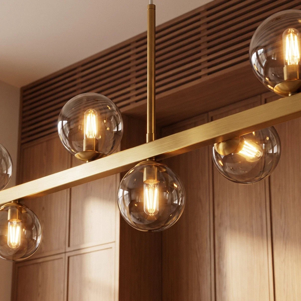 Clérachic chandelier detail shows clear glass globes and brass stems meeting the bar, filament bulbs lit warm.