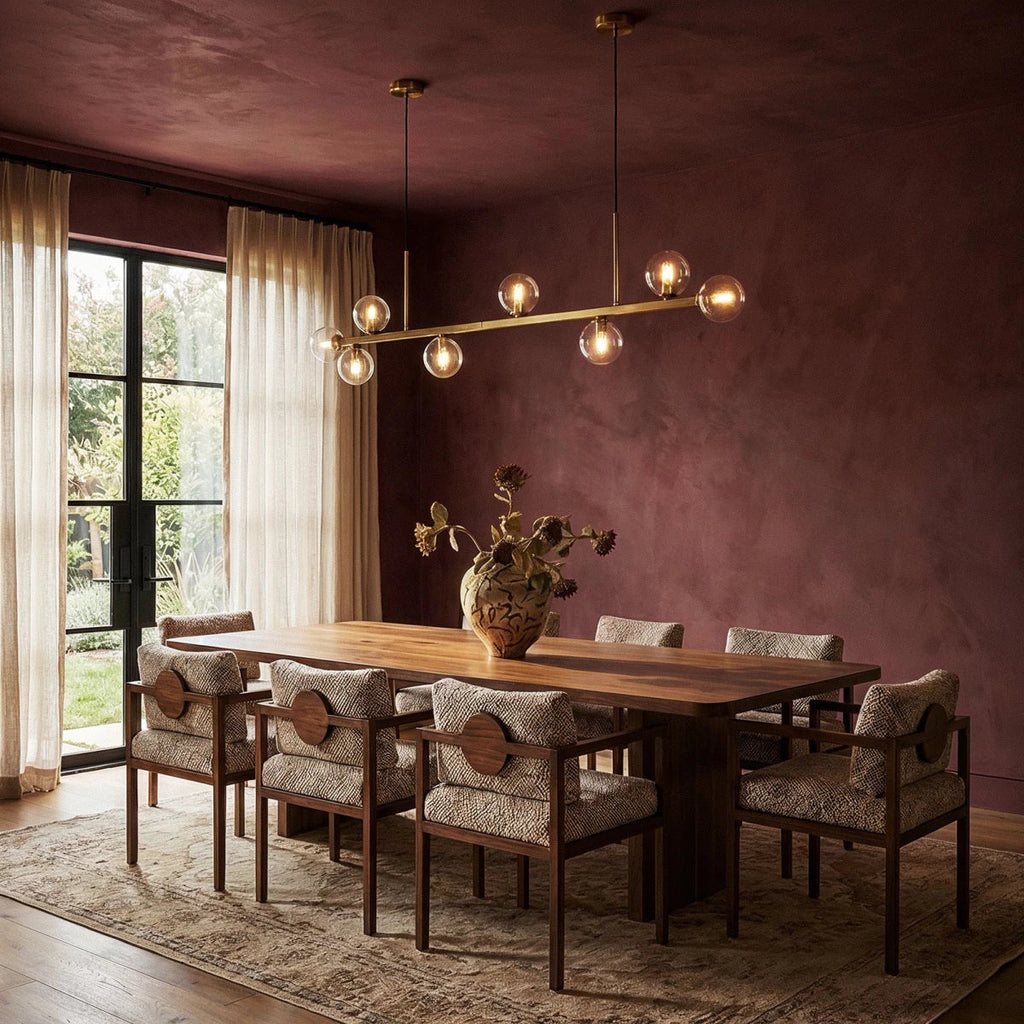Clérachic linear chandelier over a walnut dining table, clear glass globes glowing against a burgundy wall.