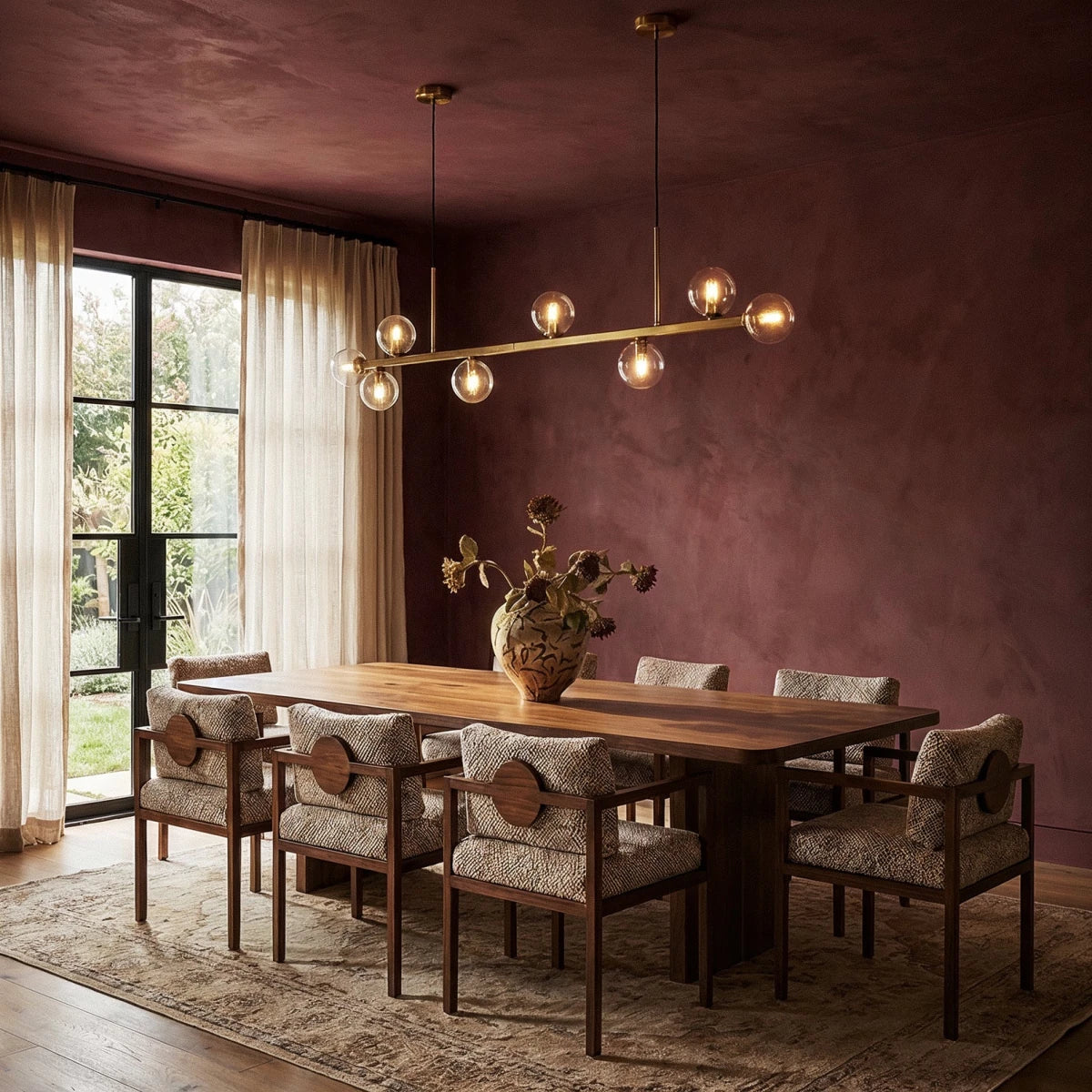 Clérachic linear chandelier over a walnut dining table, clear glass globes glowing against a burgundy wall.