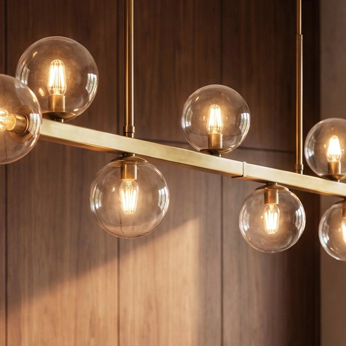 Clérachic chandelier close-up shows clear glass globes and brass stems against a wood-paneled wall.