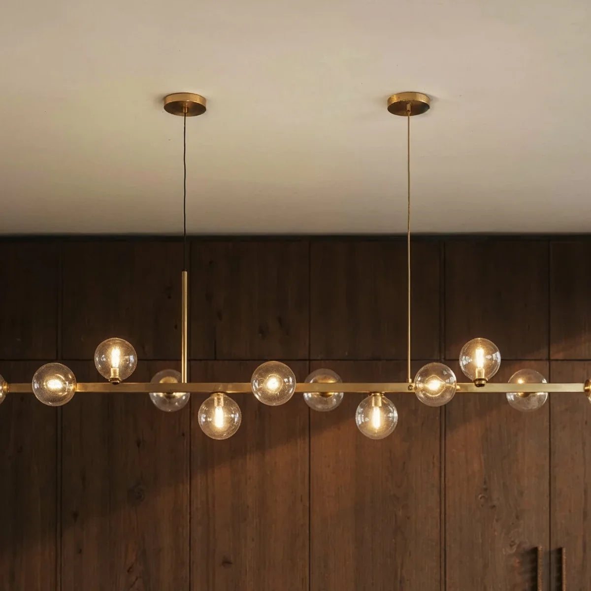 Clérachic chandelier detail shows twin round ceiling canopies and clear glass globes against wood paneling.