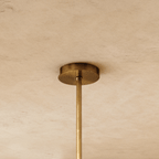 Clérachic chandelier's round brass ceiling canopy and slim brass rod seen close up against a soft limewash ceiling.