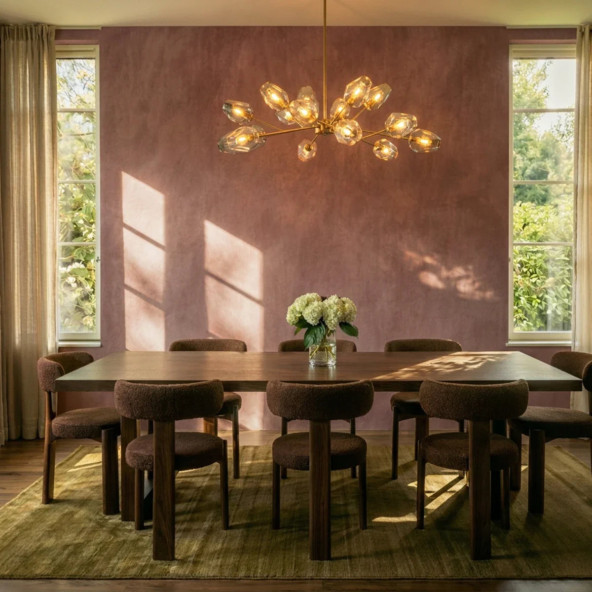 Clérachic brass chandelier with amber-tinted glass heads lit above a long walnut dining table and bouclé chairs.