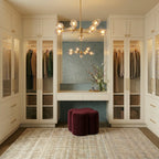 Clérachic brass chandelier glowing above a vanity stool in a walk-in wardrobe with fluted glass cabinet doors.