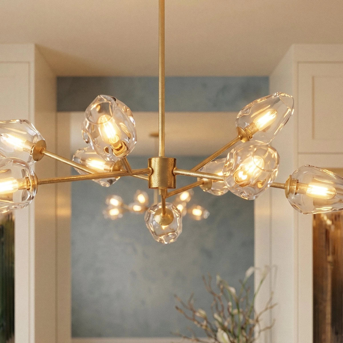 Clérachic brass chandelier close up, clear rippled glass heads with warm filament bulbs on arms from a square hub.