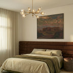 Clérachic brass chandelier lit above a bed with a rust corduroy headboard and a large landscape painting.