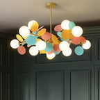 Clérachic chandelier with frosted glass globes and pastel metal discs on a brass frame, against dark green panelling.