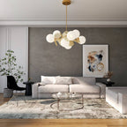 Clérachic globe-and-disc chandelier in brass, cream and frosted white, hung above a grey sofa in a living room.