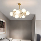 Clérachic brass chandelier with glowing frosted globes and cream discs, hung low in a grey bedroom.