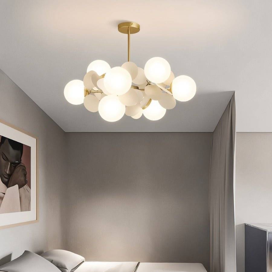 Clérachic brass chandelier with glowing frosted globes and cream discs, hung low in a grey bedroom.