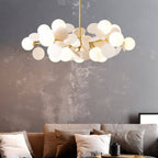 Clérachic wide chandelier of frosted glass globes and cream discs on brass arms, above a sofa and grey wall.