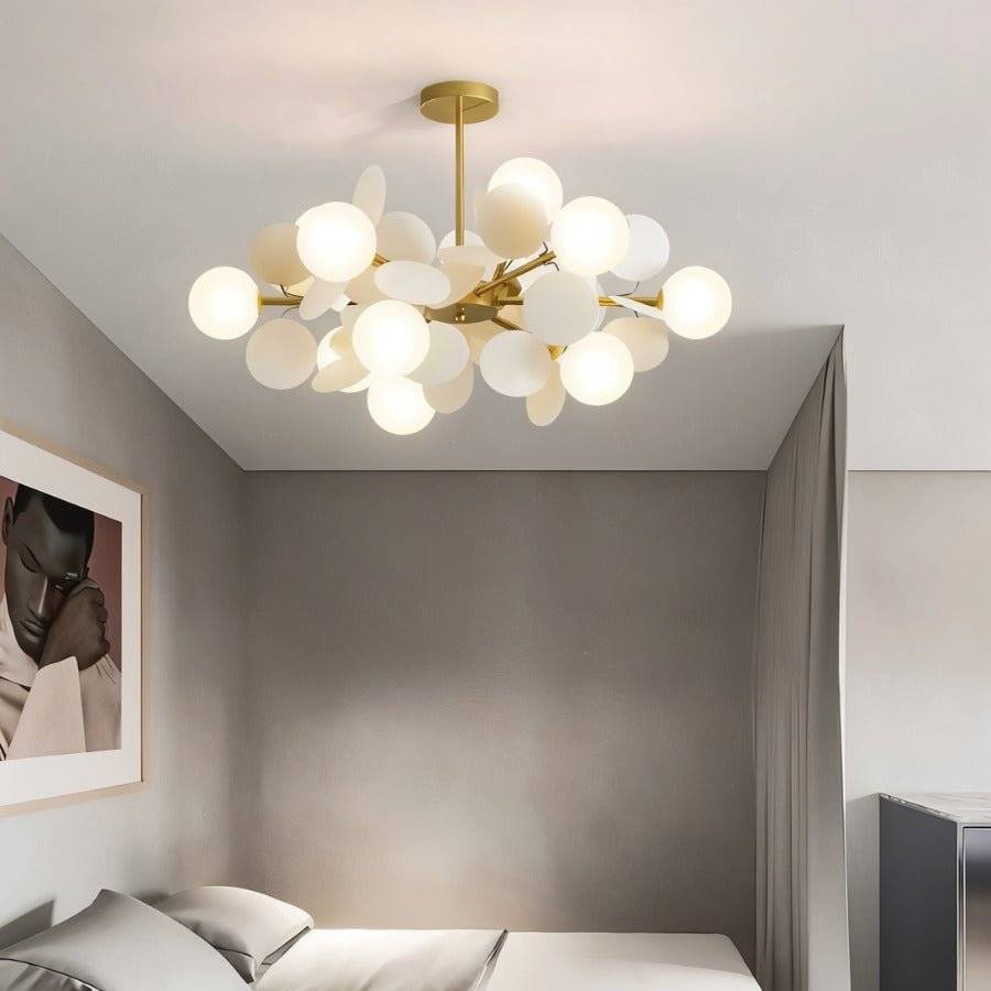 Clérachic brass chandelier of frosted glass globes and cream discs, lit above a bed in a soft grey bedroom.