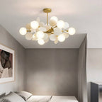 Clérachic brass chandelier of frosted glass globes and cream discs, lit above a bed in a soft grey bedroom.