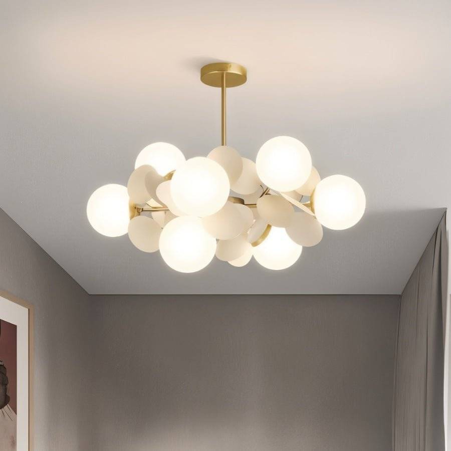 Clérachic compact brass chandelier of frosted glass globes and cream discs, lit warm against a grey room.