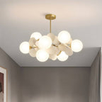 Clérachic compact brass chandelier of frosted glass globes and cream discs, lit warm against a grey room.