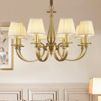 Close crop of this Clérachic brass chandelier, with curved brass arms and pleated shades, against a cream panelled wall.