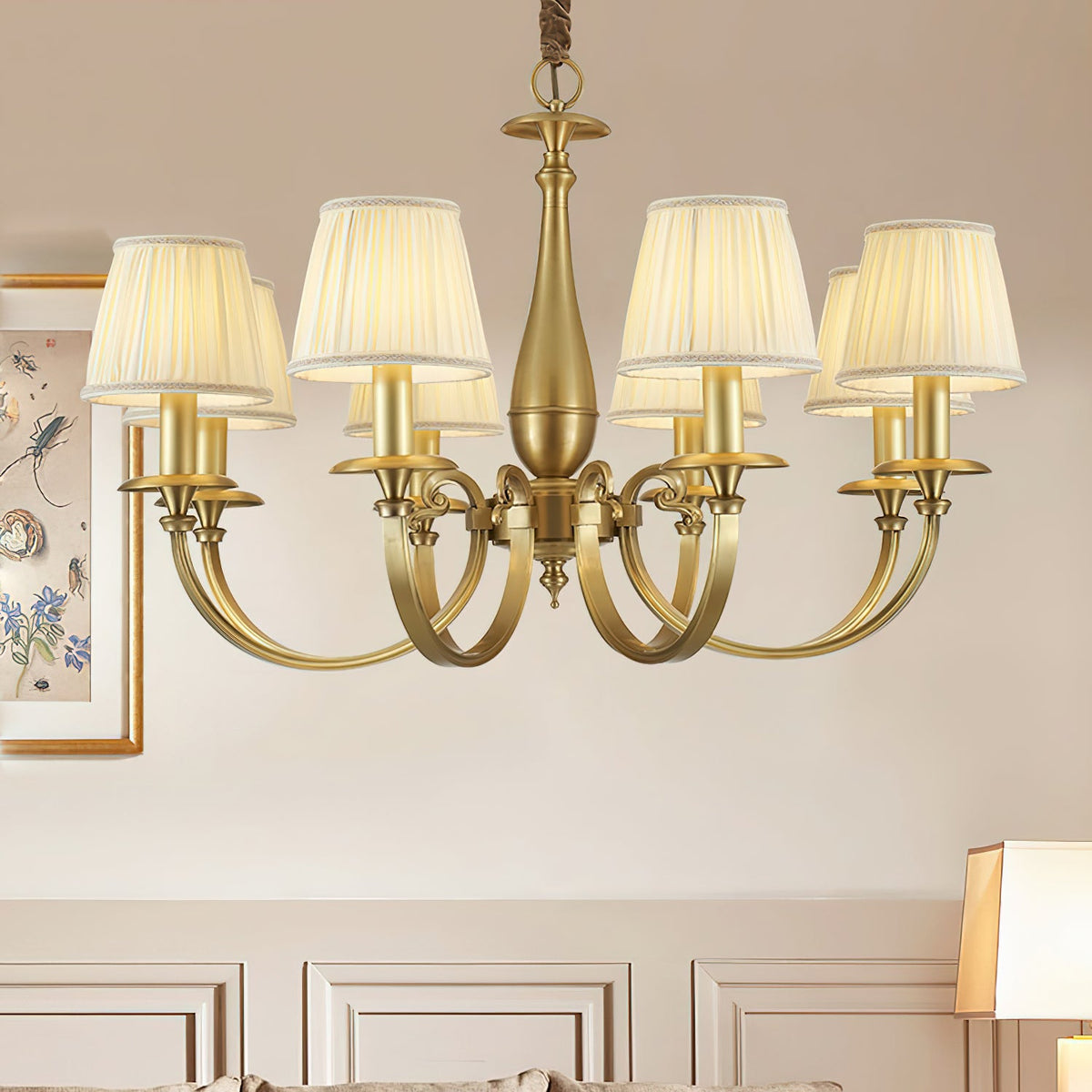Close crop of this Clérachic brass chandelier, with curved brass arms and pleated shades, against a cream panelled wall.